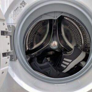 Close-up of black sneakers inside a washing machine drum showcasing laundry theme.